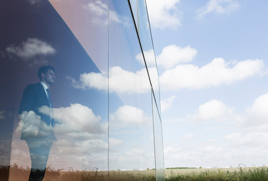 Pensive businessman looking out modern office window at blue sky clouds