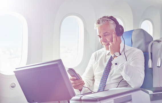 Businessman with headphones watching movie on airplane