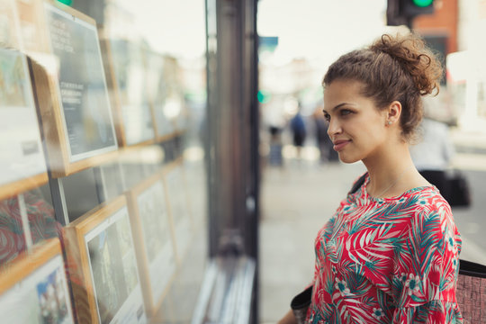 Young woman browsing real estate listings at urban storefront