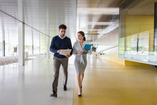 Businessman businesswoman walking discussing paperwork in modern office corridor