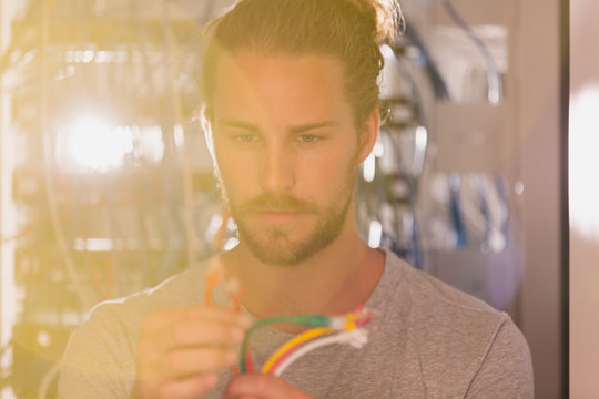 Focused IT technician examining connection plugs in server room