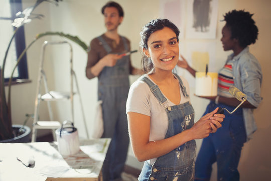 Portrait smiling young woman painting living room with friends
