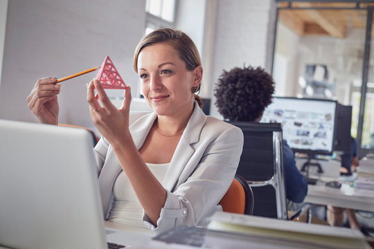 Smiling female design professional examining triangle prototype at laptop in office