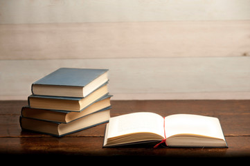 stack of books on wooden desk, with open book
