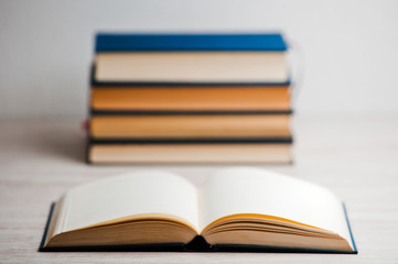 stack of books on wooden desk, with open book