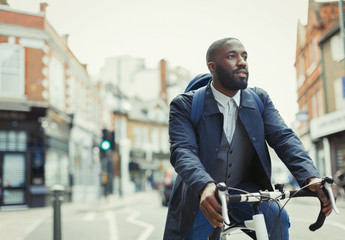 African businessman commuting, riding bicycle on urban street