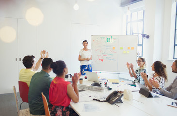 Supportive colleagues clapping for female architect leading meeting at whiteboard