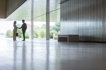 Silhouette businessman businesswoman handshaking in modern office lobby corridor