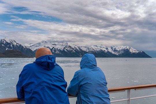 Couple on a cruise ship in Alaska. Husband and wife are enjoying an amazing view of Hubbard Glacier and iceberg. Snow peaks and ice all around in the sea.
