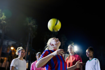 Young female soccer players practicing at night, heading the ball