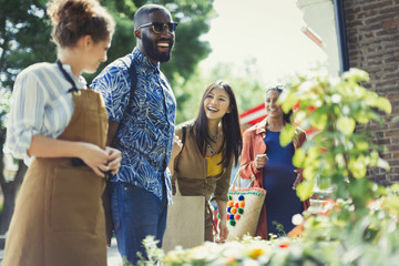 Female florist helping friends at sunny flower shop storefront