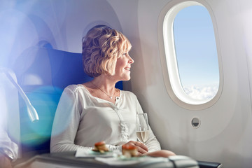 Smiling woman drinking champagne, traveling first class, looking out airplane window