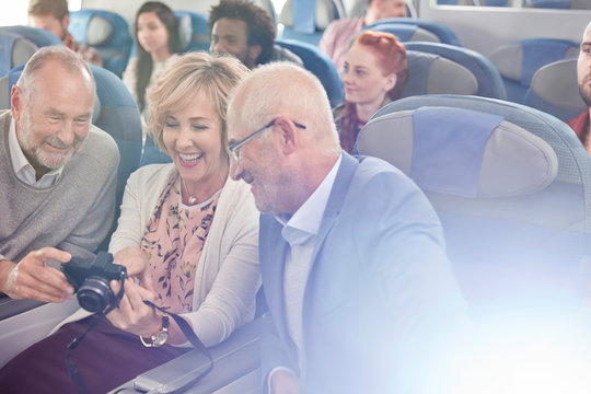 Smiling friends looking at photos on digital camera on airplane