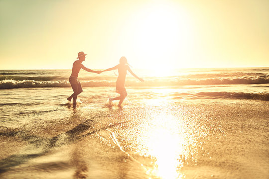Young couple holding hands, walking in sunny summer sunset ocean beach surf