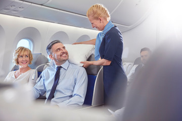 Smiling flight attendant adjusting pillow for businessman in first class on airplane