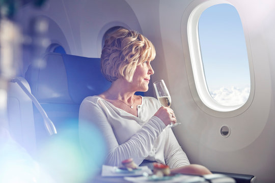 Mature woman drinking champagne, looking out window in first class on airplane