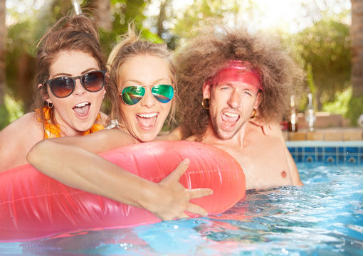 Portrait exuberant, playful young friends with inflatable raft in summer swimming pool