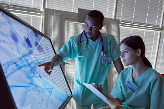 Nurses clipboard examining magnified microscope slide on computer monitor