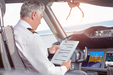 Male pilot with clipboard preparing in airplane cockpit