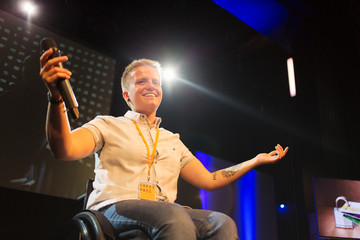 Smiling, confident female speaker with microphone in wheelchair on stage