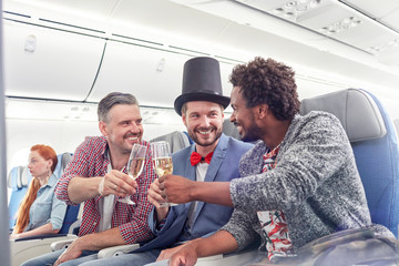 Young male friends toasting champagne glasses in first class on airplane