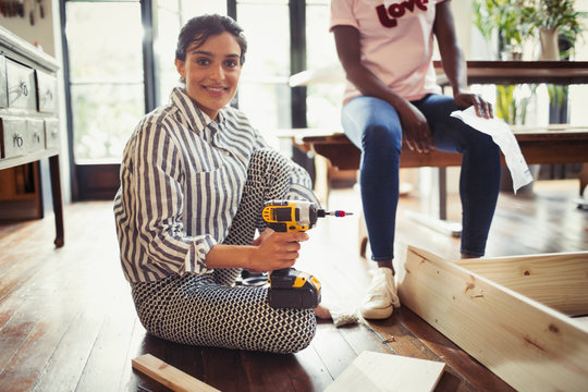Portrait smiling woman with power drill assembling furniture