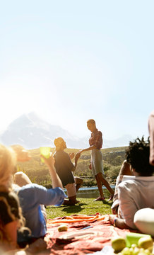 Friends watching young man proposing to woman at sunny summer picnic