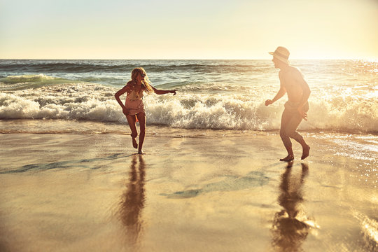 Playful young couple running in wet sand on sunny summer ocean beach
