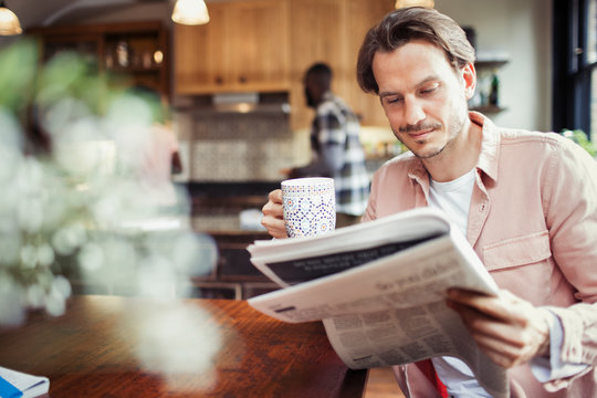 Man drinking coffee and reading newspaper in kitchen