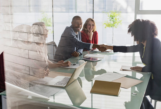 Businessman businesswoman handshaking across conference table in meeting