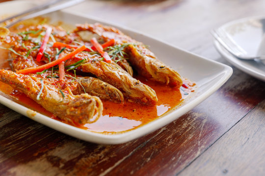 Close up view of Spicy Red Curry with crispy fried soft fish, Sheatfish, on white dish and wooden table. 