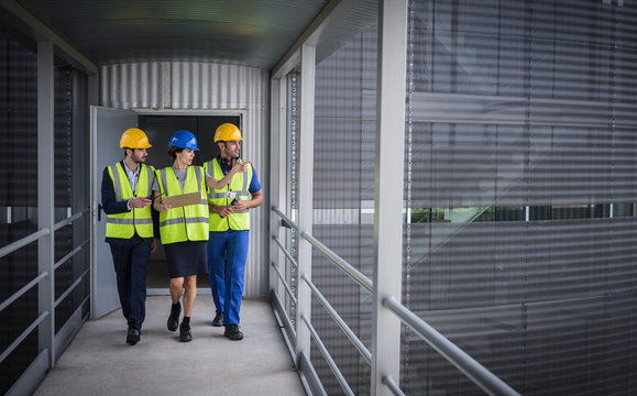 Supervisors with clipboard walking and talking on elevated walkway outside factory