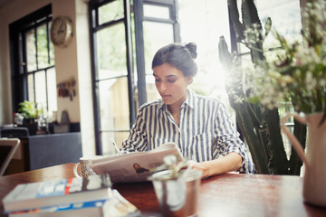 Young woman with newspaper at dining room