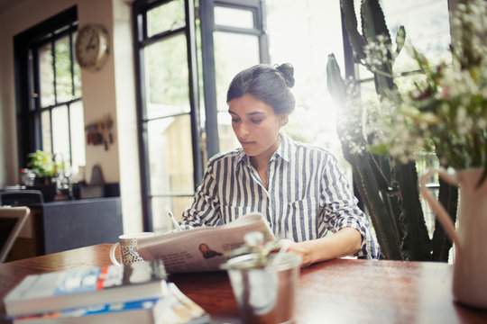 Young woman with newspaper at dining room