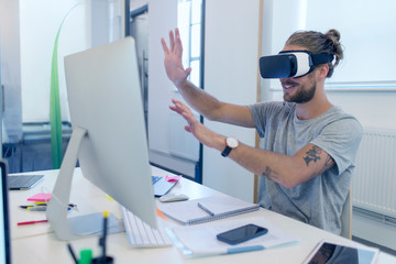 Male computer programmer programming virtual reality simulator glasses at computer in office