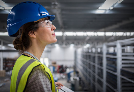 Smiling, confident female supervisor in hard-hat looking up in factory