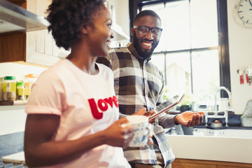 Young couple drinking coffee and using digital tablet in kitchen