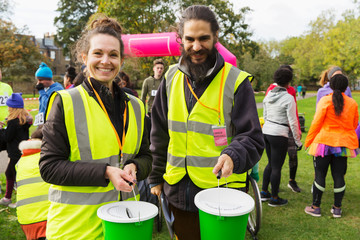 Portrait smiling volunteers donation buckets at charity run in park