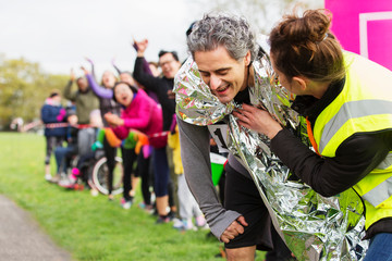 Woman wrapping thermal blanket around exhausted male runner finishing marathon
