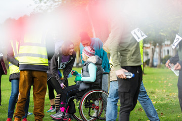 Woman in wheelchair talking to friends at charity race in park
