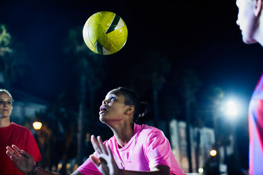 Young female soccer player heading the ball on field at night