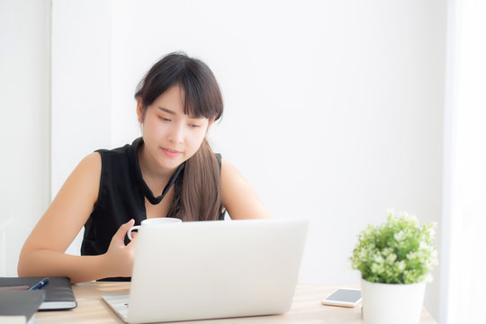 Beautiful freelance asian woman smiling working and typing on laptop computer at desk office with professional, girl using notebook checking email or social network, business and lifestyle concept.