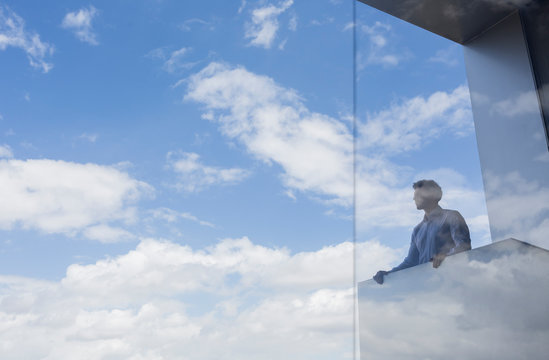 Pensive businessman standing at modern balcony looking at sunny blue sky clouds