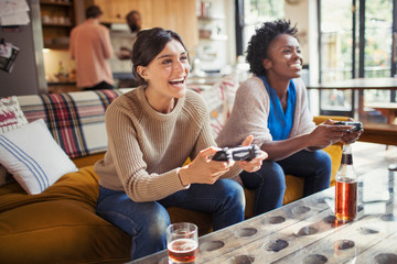 Laughing women friends playing video game on living room sofa
