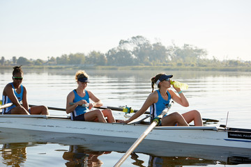 Female rowing team resting, drinking water in scull on sunny lake