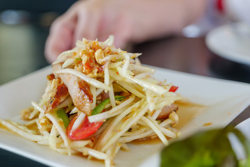 Close up view of Thai spicy green papaya salad, Som Tum, with Grilled pork neck and background of hand hold the white plate.