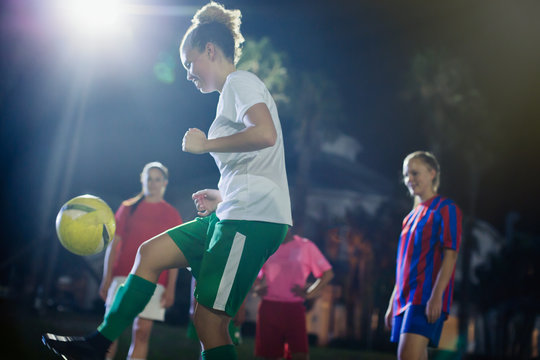 Young female soccer player kicking the ball, practicing on field at night