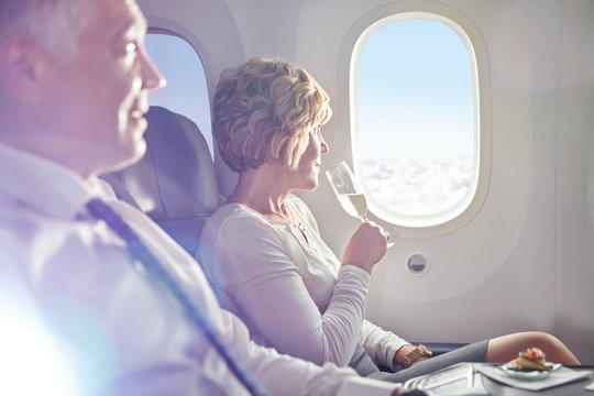 Woman drinking champagne in first class, looking out airplane window