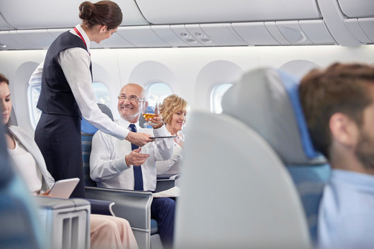 Flight attendant serving whiskey to businessman in first class on airplane