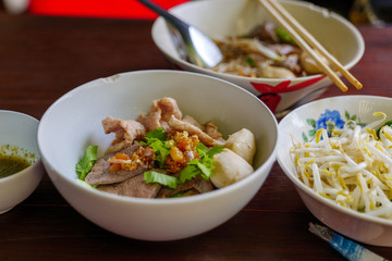 Close up view of Spicy Thai Boat rice Noodle Soup,  Kuai Tiao Ruea, serve on ceramic bowl on wooden table with fresh bean sprouts on side. 